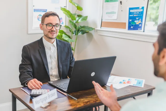 A mortgage broker and client discussing loan options in a modern office setting. Are lead generation companies for mortgage brokers worth the cost?