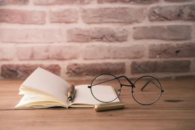 Round glasses, open book, and pen on a desk against brick wall. Vintage style. Lead generation marketplace due diligence for UK buyers: records to request