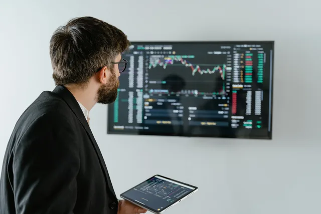 A businessman examines stock market data displayed on a monitor, holding a tablet. Three bounded AI applications for lead networks, tested before the tool is bought