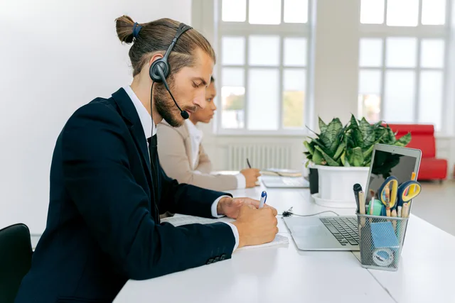 Customer service representative with headset working at office desk. Professional workspace environment. Eight fixtures to test lead network attribution methods before reporting