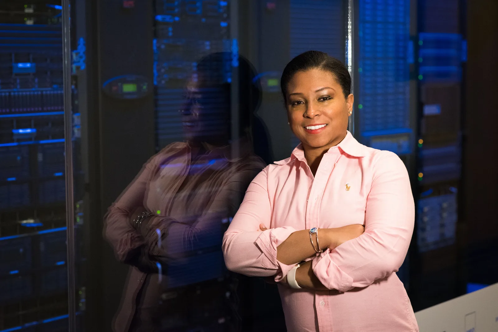 Smiling IT professional with crossed arms in a server room, reflecting her expertise.