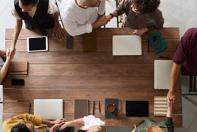 Group of adults having a business meeting, discussing plans around a wooden table with tech devices. How to estimate England's lead network opportunity from a population frame and labelled inputs