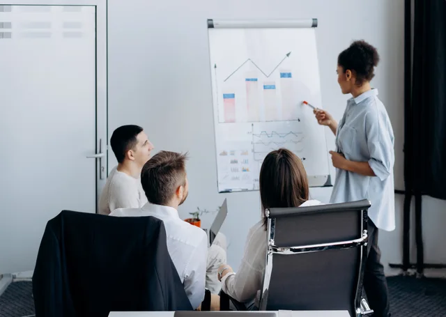 Business team in meeting with presenter discussing charts on a flip board. Comparing lead network pricing models by unit, whole-life cost and dispute rights